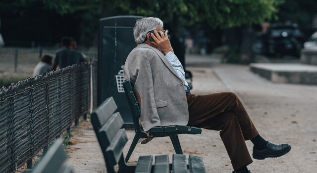 Elderlymansittingonbenchtalkingonphone
