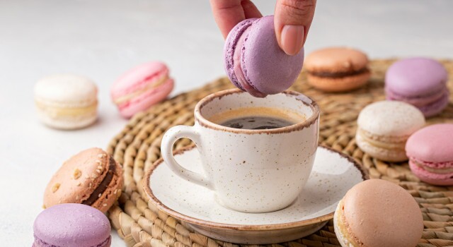 Persondippingmacaroonsintocupofcoffeeonawickertray